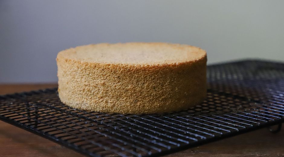 A freshly baked sponge cake resting on a cooling rack, showcasing its golden crust.